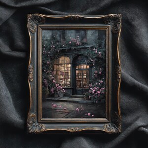 May include: A framed artwork depicts a quaint bookstore facade, illuminated from within. The building is draped in climbing roses with pink blossoms. The ornate, dark-toned frame adds a vintage aesthetic to the scene.