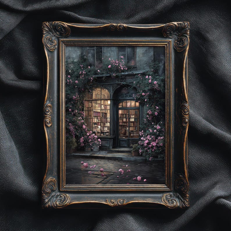 May include: A framed artwork depicts a quaint bookstore facade, illuminated from within. The building is draped in climbing roses with pink blossoms. The ornate, dark-toned frame adds a vintage aesthetic to the scene.