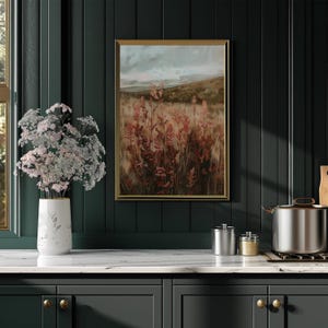 May include: A framed landscape painting with a gold frame depicts a field of tall, reddish-brown plants under a cloudy sky. A white vase with pink flowers sits on a white countertop. The background is a dark green wall.