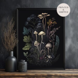K&ouml;nnte beinhalten: Ein gerahmter botanischer Druck mit einer detaillierten Illustration von Pilzen und Pflanzen in ged&auml;mpften Gr&uuml;n-, Braun- und Cremet&ouml;nen vor einem schwarzen Hintergrund. Das Kunstwerk wird auf einer Holzoberfl&auml;che mit zwei dunklen Vasen pr&auml;sentiert.