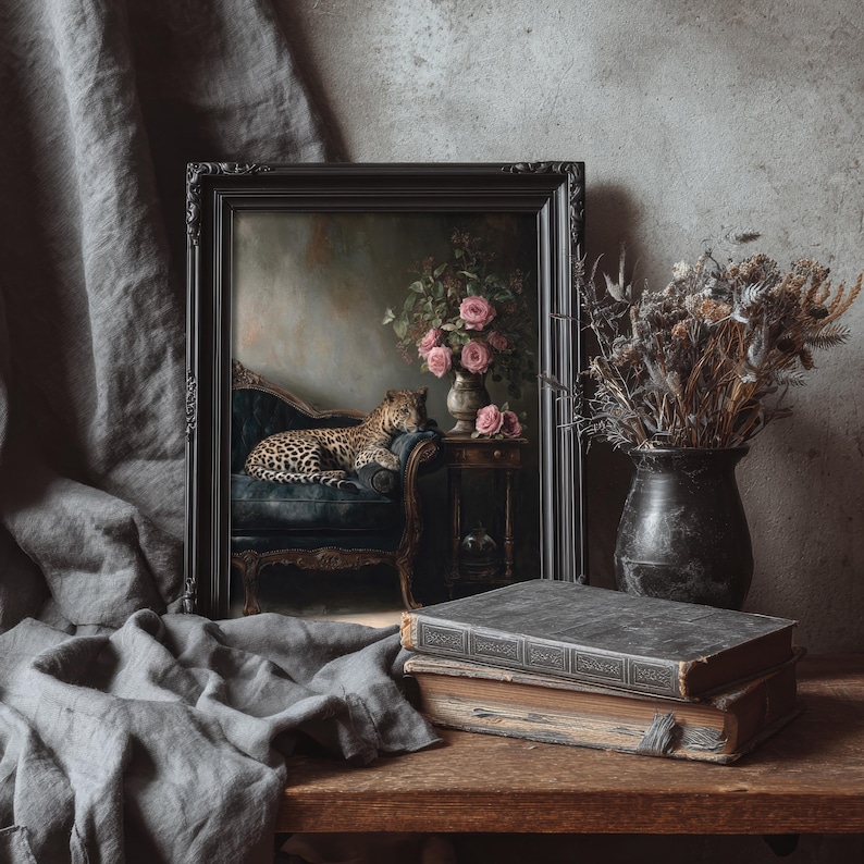 May include: A black framed painting depicting a leopard on a blue chaise longue, with pink roses in a vase. The painting is on a wooden table with two antique books and a vase of dried flowers.