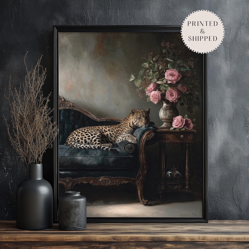 May include: A framed art print depicting a leopard reclining on a dark blue chaise longue. A vase of pink roses sits on a small table. The artwork has a vintage aesthetic with a dark, moody colour palette.