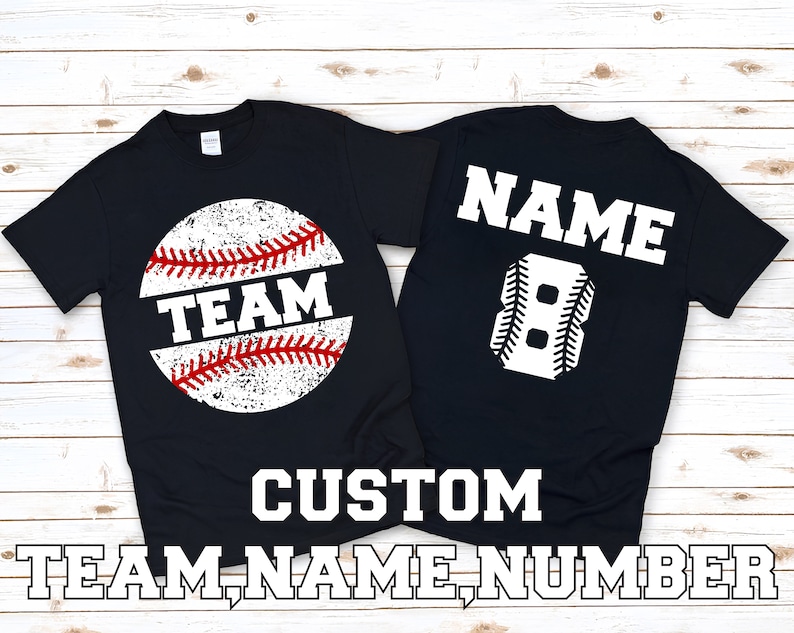 May include: Two black t-shirts with a baseball theme. The front of one shirt has a white baseball with red stitching and the word "TEAM" in red. The back of the other shirt has a white baseball-shaped number "8" and the word "NAME" in white.