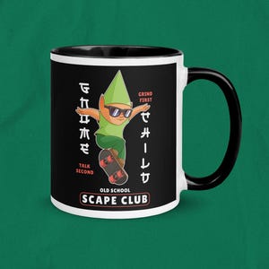 Op de afbeelding: Zwart-witte keramische mok met een zwart handvat en interieur. De mok heeft een cartoon dwerg die skateboardt, een zonnebril draagt en de tekst "GRIND FIRST, TALK SECOND, OLD SCHOOL SCAPE CLUB."