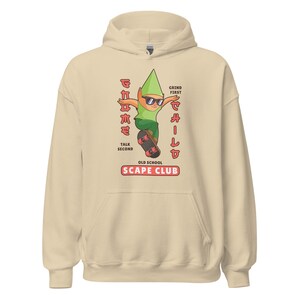Puede incluir: Una sudadera con capucha beige con un personaje de dibujos animados haciendo skateboard. El personaje lleva gafas de sol y un sombrero verde. El texto en la sudadera dice "Grind First Chill Second Old School Scape Club".