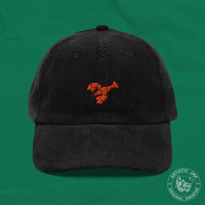 May include: Black corduroy baseball cap with an orange geometric design. The cap features a curved peak and a classic six-panel design. The cap has an orange geometric design on the front.