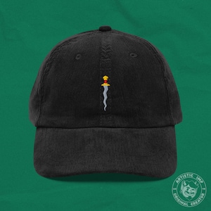 May include: Black corduroy baseball cap featuring an embroidered dagger design in yellow, red, and white. The cap has a curved peak and a structured crown. A fashionable accessory.