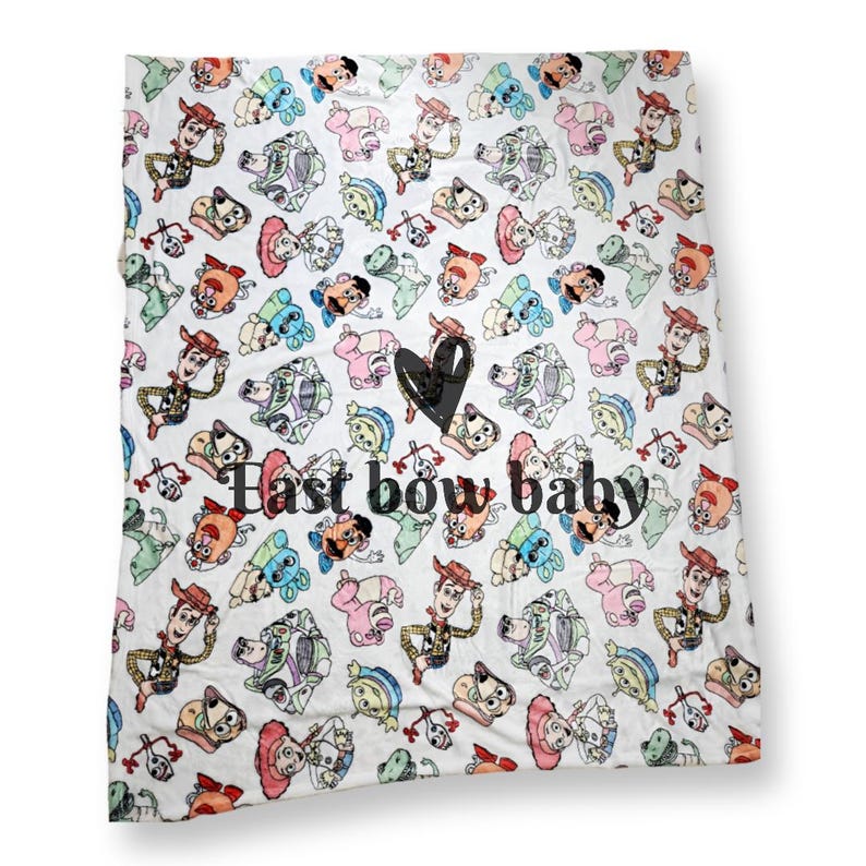 Może przedstawiać: Biały koc z polaru z powtarzającym się wzorem postaci z Toy Story. Koc ma napis "Last bow baby" czarnymi literami.