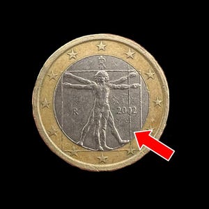 May include: A gold-colored coin with a silver center featuring a drawing of a man in a square frame. The coin has 12 stars around the edge and the year 2002 printed on the silver center.