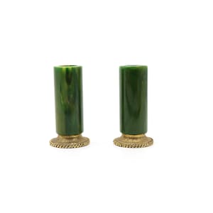 May include: A pair of cylindrical candle holders featuring a marbled dark green body with a smooth finish. Each holder is supported by a circular, textured gold-toned metal base with a rope-like pattern along the outer edge of the rim.