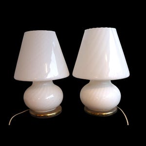 Puede incluir: Dos lámparas de mesa de vidrio blanco con diseño de espiral en la base y la pantalla. Las lámparas tienen una base dorada y una forma clásica de hongo. Sobre un fondo negro.