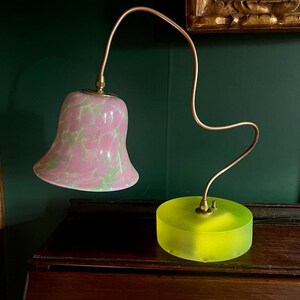 May include: A pink and green glass lampshade with a copper-colored flexible arm and a yellow glass base.