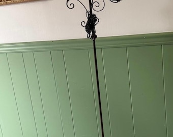 May include: An antique floor lamp with a dark metal frame and a white glass globe shade. The lamp features decorative scrollwork and a slender, vertical design. The base has a three-footed design. The lamp is a vintage lighting fixture.