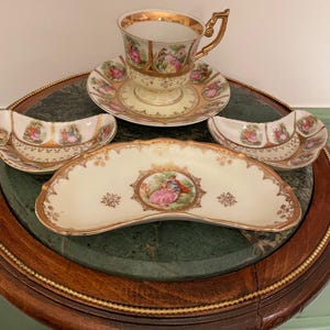 May include: A vintage porcelain tea set with a gold trim and floral patterns. The set includes a cup, saucer, and two small dishes.