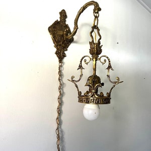 May include: A brass wall-mounted light fixture with a chain and a white light bulb. The fixture has a decorative design with ornate details.