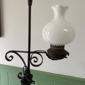 May include: A vintage floor lamp with a white glass shade and a dark brown metal frame. The lamp features a decorative, scrolled arm and a round, bulbous shade. The lamp's base is not visible.
