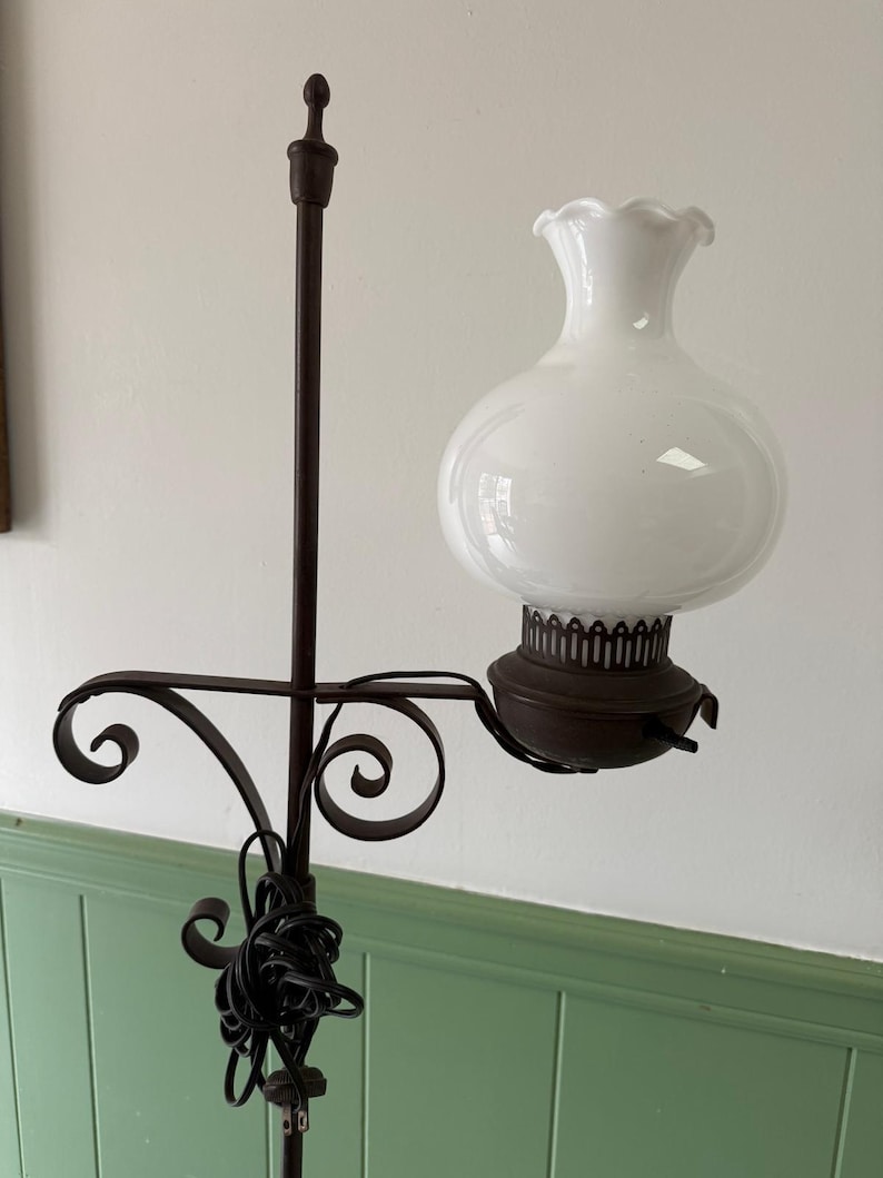 May include: A vintage floor lamp with a white glass shade and a dark brown metal frame. The lamp features a decorative, scrolled arm and a round, bulbous shade. The lamp's base is not visible.