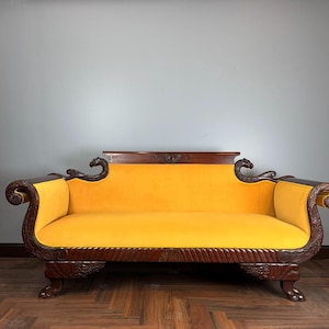 May include: A vintage yellow velvet sofa with dark wood detailing. The sofa has elaborate carvings on the arms and legs, and a decorative back. This sofa is a classic piece of furniture.