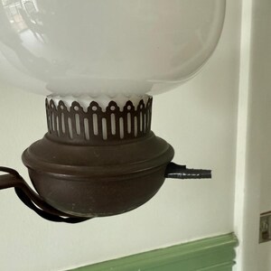 May include: An antique oil lamp with a large, frosted glass globe. The lamp features a dark brown metal base and a decorative, scalloped edge. The lamp is suspended from a curved metal arm.