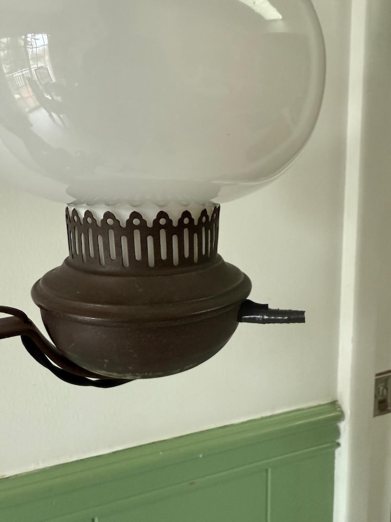 May include: An antique oil lamp with a large, frosted glass globe. The lamp features a dark brown metal base and a decorative, scalloped edge. The lamp is suspended from a curved metal arm.