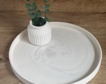 May include: White round tray with a marbled design and a small white vase with green plant stems on top.