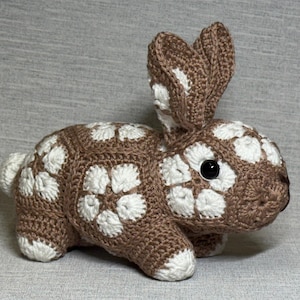 May include: A crocheted brown and white rabbit with a flower pattern. The rabbit has a black button eye.