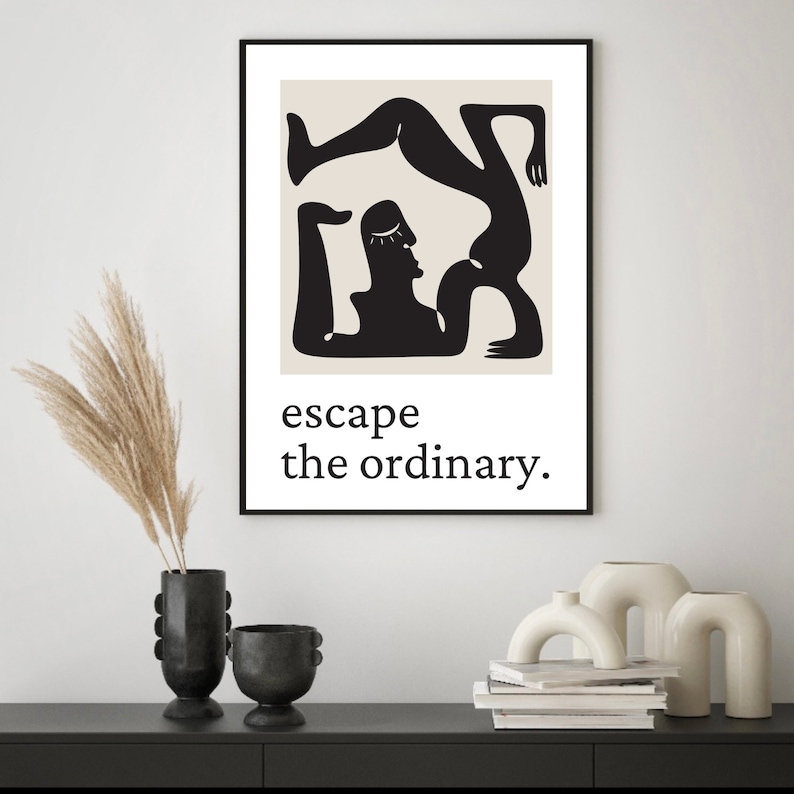 May include: Black and white minimalist art print featuring two figures in a yoga pose. The print has a beige background and the text "escape the ordinary."