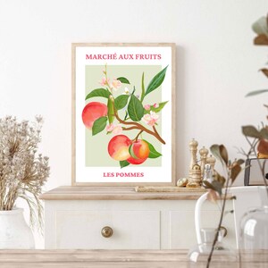 May include: A vintage-style poster with a green background featuring a branch of a fruit tree with red apples and pink blossoms. The text "MARCH&Eacute; AUX FRUITS" and "LES POMMES" is printed in pink.