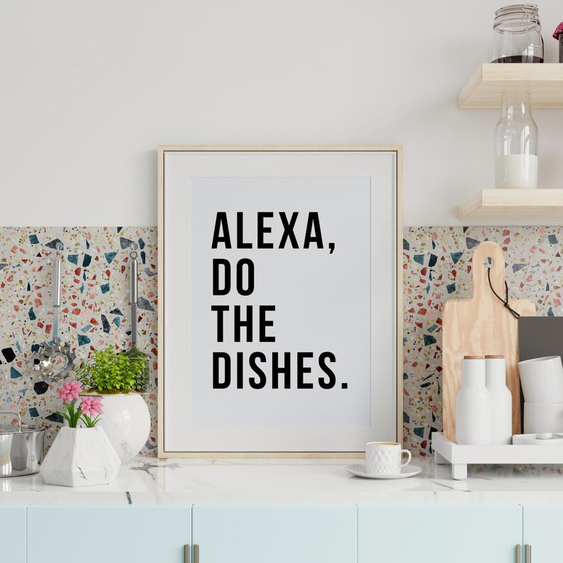 May include: A white framed print with black text that reads "ALEXA, DO THE DISHES." The print is hanging on a wall with a colorful tile backsplash.