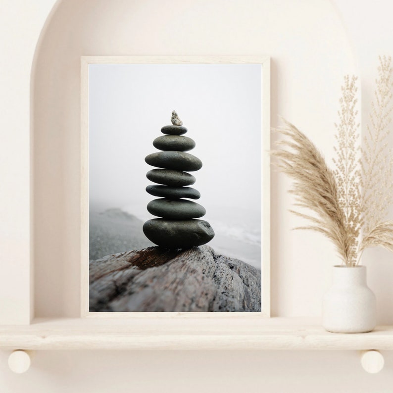 May include: A stack of gray stones balanced on top of a weathered piece of driftwood against a foggy background.