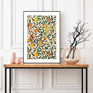 K&ouml;nnte beinhalten: Ein gerahmter Druck eines Vintage-Blumenmusters mit einem sich wiederholenden Design aus gr&uuml;nen Bl&auml;ttern, orangefarbenen und gelben Fr&uuml;chten und wei&szlig;en Bl&uuml;ten auf einem hellrosa Hintergrund.