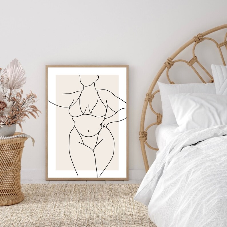 May include: A line drawing of a person in a swimsuit, with a beige background. The drawing is in black and white and is framed in a light wood frame.