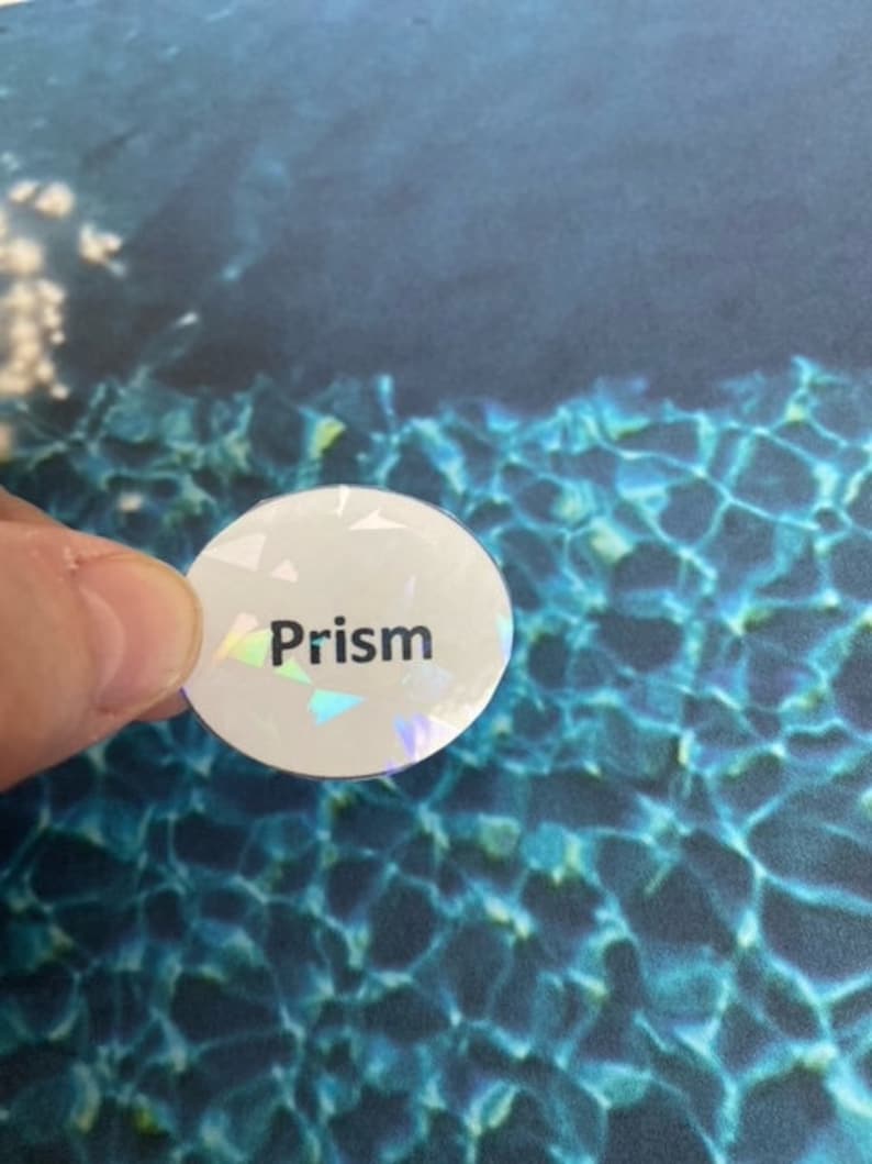 May include: A round, white sticker with the word "Prism" printed in black. The sticker has a holographic, iridescent finish. The background is a blue and teal water pattern.