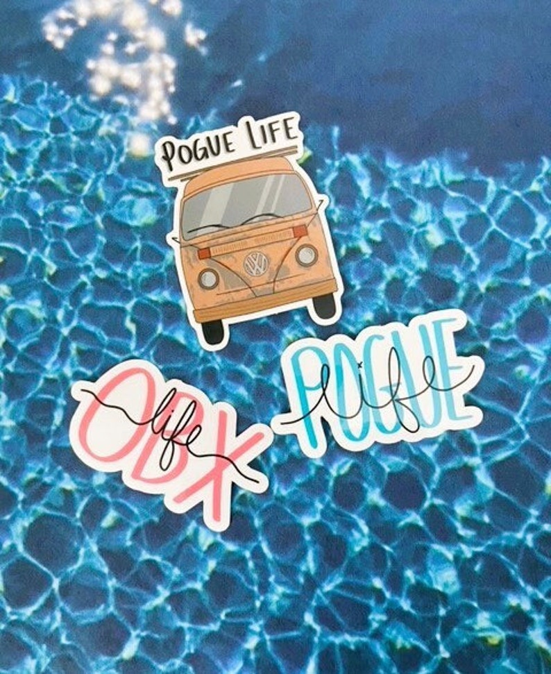 May include: Three stickers with a beach theme. The first sticker is a cartoon of a vintage van with the text "Pogue Life" above it. The second sticker is the text "OBX Life" in pink and black. The third sticker is the text "Pogue Life" in blue and black.