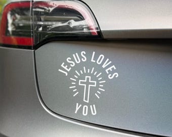 May include: A white vinyl decal with the text "JESUS LOVES YOU" and a cross design, affixed to the rear of a gray car. The car's taillight and a license plate are also visible.