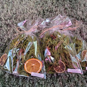 May include: Two clear plastic bags filled with dried greenery and orange slices. The bags are tied with twine and have a pink label with the text "Off Grid Sushi" and "www.offgridsushi.com".
