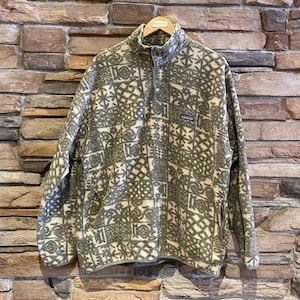May include: A green and white patterned fleece pullover with a snap button closure at the neck. The fleece has a geometric pattern and the brand name "Patagonia" is visible on the left chest.