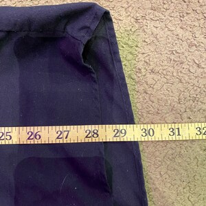 K&ouml;nnte beinhalten: Nahaufnahme eines dunkelblauen Stoffes mit einer Naht entlang der Kante. Ein Ma&szlig;band ist entlang der Unterkante des Stoffes gelegt und zeigt Ma&szlig;e von 25 bis 32 Zoll.