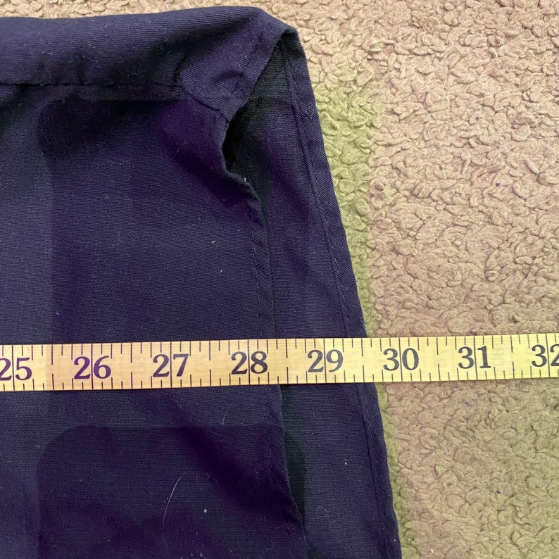 K&ouml;nnte beinhalten: Nahaufnahme eines dunkelblauen Stoffes mit einer Naht entlang der Kante. Ein Ma&szlig;band ist entlang der Unterkante des Stoffes gelegt und zeigt Ma&szlig;e von 25 bis 32 Zoll.