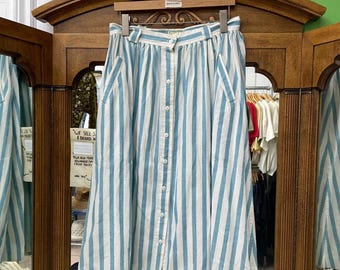 May include: A vintage knee-length skirt with vertical stripes in light blue and white. The skirt has a button-down front, pockets, and a high waist. The skirt is hanging on a wooden hanger in front of a mirror.