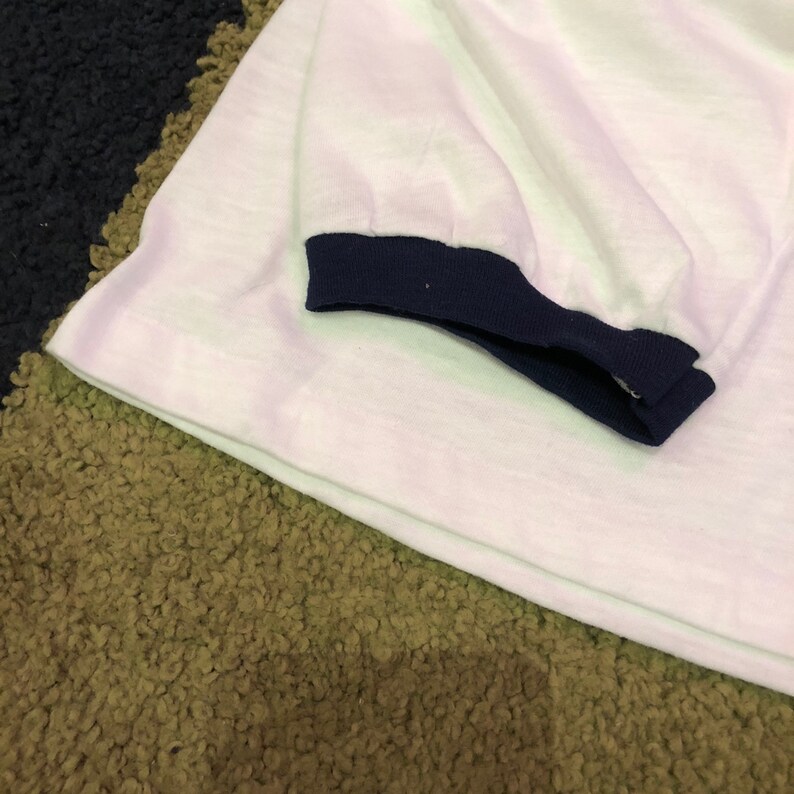 May include: White t-shirt with a navy blue ribbed trim around the sleeves.