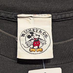 May include: A white ceramic mug with a black handle and the text "But First, Coffee" in a bold, black font. The mug is set against a blurred background, suggesting a cosy setting.