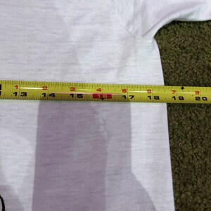 May include: A white t-shirt with a yellow measuring tape laid across it. The tape measures 16 inches.
