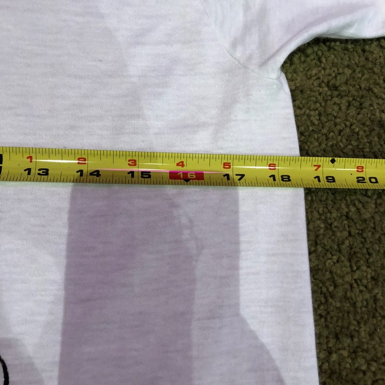 May include: A white t-shirt with a yellow measuring tape laid across it. The tape measures 16 inches.