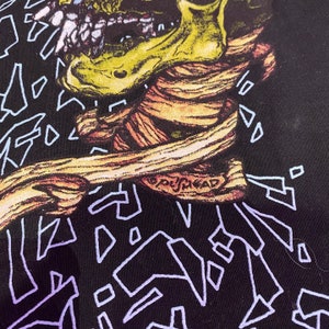K&ouml;nnte beinhalten: Schwarzes T-Shirt mit einem grafischen Druck eines Skeletts mit einem gelben Sch&auml;del und rotem und orangefarbenem Muskelgewebe. Der Text "GHOSTHEAD" ist auf den Hals des Skeletts gedruckt. Der Hintergrund ist schwarz mit einem Muster aus violetten und blauen geometrischen Formen.