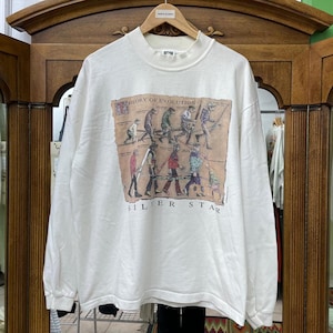 May include: White long-sleeve sweatshirt with a mock turtleneck. The front features a graphic depicting the evolution of humans, with the text "THEORY OF EVOLUTION" and "SILVER STAR". The sweatshirt is hanging on a wooden hanger.