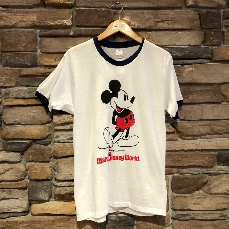 May include: White t-shirt with a blue ringer neck and a vintage Mickey Mouse graphic. The shirt says "Walt Disney World."