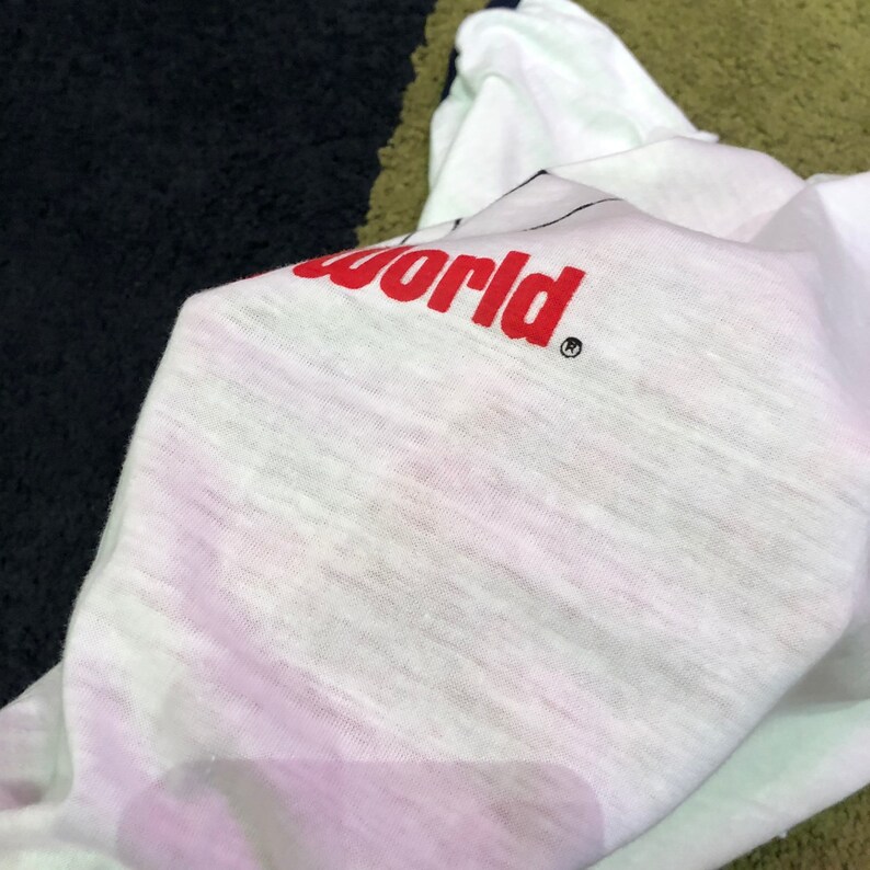 May include: White t-shirt with red text that reads "World" with a registered trademark symbol.