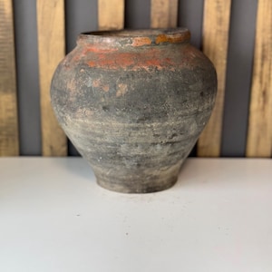 Puede incluir: Una olla grande de cerámica gris oscuro con una abertura ancha y un fondo ligeramente redondeado. La olla tiene un borde marrón rojizo y está hecha de arcilla rugosa y texturizada.