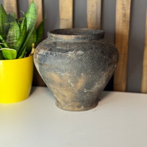 Peut inclure: Un vase en céramique brun foncé avec une finition vieillie. Le vase a une large ouverture et un corps arrondi.